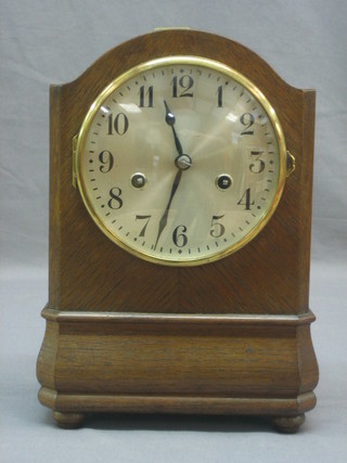 A striking mantel clock with silvered dial and Arabic numerals contained in an oak arch shaped case