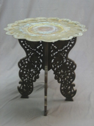 A circular benares brass table, raised on a pierced  folding hardwood stand 24"