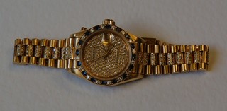 A lady's Rolex Oyster Dayjust wristwatch contained in an 18ct Swiss gold case with integral bracelet, the bezel set numerous diamonds and sapphires, complete with original box 