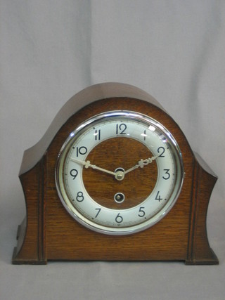 An Art Deco 8 day mantel clock with silvered dial and Arabic numerals, contained in an oak arch shaped case