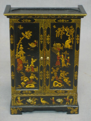 A dolls house black lacquered chinoiserie style wardrobe with moulded cornice enclosed by a panelled door, the base fitted a drawer and raised on bracket feet 4 1/2" together with a matching coat hanger