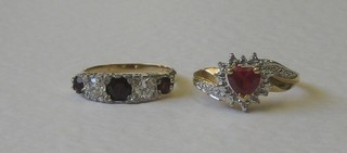 A gold dress ring set 3 red stones and 2 white stones and 1 other gold dress ring set a heart shaped red stone surrounded by white stones
