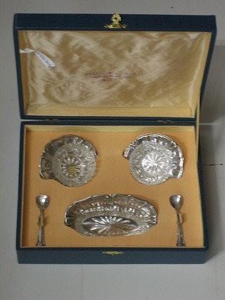 A pair of circular Continental cut glass salts raised on silver trays, an oval butter dish and 2 matching spoons, cased