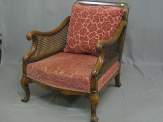 A pair of carved walnut single cane bergere chairs, raised on cabriole supports