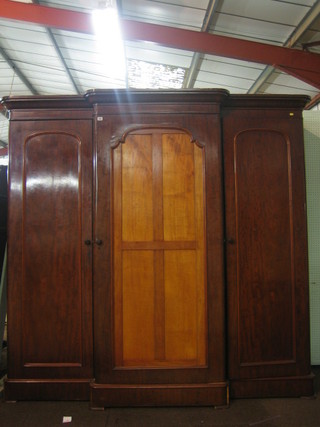 A Victorian mahogany triple wardrobe with moulded cornice, the centre section fitted trays above 3 long drawers enclosed by an arch panelled door, flanked by a pair of cupboards enclosed by arch panelled doors, raised on a platform base 86"