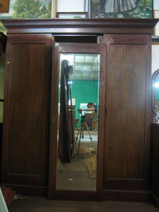 A Victorian mahogany triple wardrobe with moulded and dentil cornice enclosed by a bevelled plate mirror panelled door to the centre, flanked by a pair of panelled doors, 74"