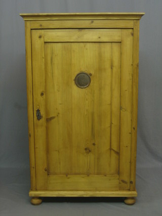 A Continental stripped and polished pine cabinet with moulded cornice enclosed by a panelled door, raised on bun feet 32"