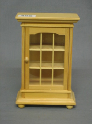 A dolls house pine display cabinet, fitted shelves enclosed by a glazed panelled door 4 1/2"