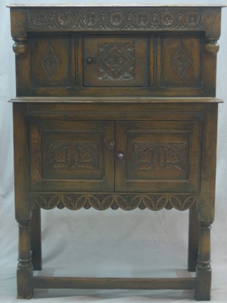 A 1930's carved oak Jacobean style court cupboard, with carved frieze, the base fitted a cupboard enclosed by double panelled doors, raised on turned and block supports 32"