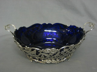 A handsome oval pierced Continental silver twin handled dish, raised on scrolled feet, complete with blue glass liner 19ozs