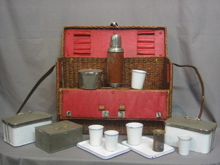 A 1930's travelling picnic hamper comprising 5 graduated enamelled beakers, 6 rectangular enamelled plates 8", 2 rectangular enamelled and chrome containers, a rectangular metal sandwich box, a Thermos flask and a folding Primus stove, all contained in a wicker carrying case