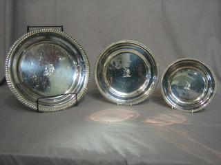 3 graduated circular silver plated platters with armorial decoration, raised on 3 bun feet