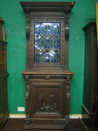A Victorian carved oak cabinet on cabinet, the upper section fitted a cupboard enclosed by a lead glazed stained glass panelled door, the base fitted a drawer above cupboard, 36"