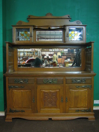 A handsome Art Nouveau honey oak Voisy style sideboard, the raised mirrored back fitted cupboards enclosed by lead glazed panelled doors with galleried decoration to the side above 3 long drawers, raised on bracket feet 72"