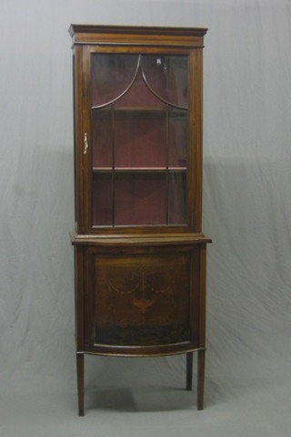 An Edwardian inlaid mahogany display cabinet, the upper section with moulded cornice, fitted shelves enclosed by astragal glazed panelled doors, the base of bow front outline enclosed by an inlaid panelled door, raised on square tapering supports 26"