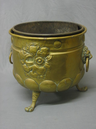 A circular Continental embossed brass coal bin with lion mask handles, raised on 3 hoof supports 15"
