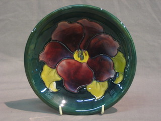 A Moorcroft Clematis pattern circular green glazed plate, the reverse with Moorcroft signature and paper label 7"