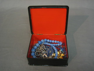 A quantity of costume jewellery contained in a red lacquered box with hinged lid