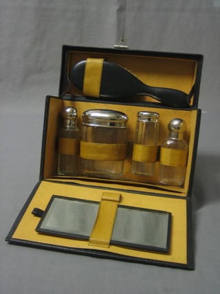 A travelling case comprising 4 cut glass bottles with silver plated tops, a mirror and a hair brush