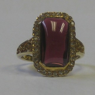 A lady's 18ct yellow gold dress ring set a cabouchon cut garnet surrounded by diamonds
