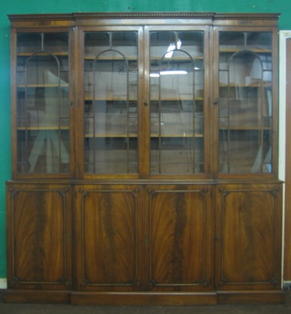 A Georgian style mahogany breakfront bookcase on cabinet, the upper section with moulded and dentil cornice, the interior fitted adjustable shelves, the base fitted cupboards enclosed by panelled doors raised on a platform base 79"