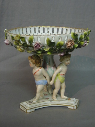 A Continental circular pierced porcelain table centre piece with floral encrusted decoration supported by 3 cherubs, raised on a triform base, 9"