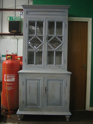 A Continental blue painted cabinet with moulded cornice, the interior fitted shelves enclosed by astragal glazed panelled doors, the base fitted a double cupboard, raised on bun feet 38"