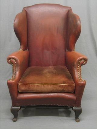 A Georgian style oak framed wing back armchair upholstered in brown rexine, raised on cabriole supports
