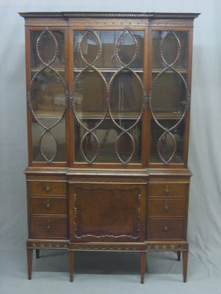 An Edwardian Chippendale style mahogany break front bookcase on cabinet, the upper section with moulded and dentil cornice and blind fret work frieze fitted adjustable shelves and enclosed by astragal glazed panelled doors, the base fitted a cupboard flanked by 6 short drawers, raised on square tapering supports ending in spade feet 42"