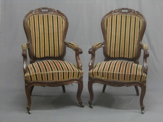 A pair of Victorian Continental carved walnut open arm chairs, upholstered in striped material, raised on cabriole supports