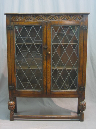 A carved oak display cabinet, the interior fitted adjustable shelves enclosed by a lead glazed panelled door, raised on turned and block supports 37"