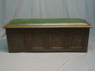 A carved oak coffer/ottoman with upholstered seat and hinged lid, having carved panelled decoration to the front and with iron drop handles to the sides 54"