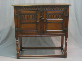 A carved oak cabinet enclosed by 2 panelled doors, raised on turned and block supports 36"