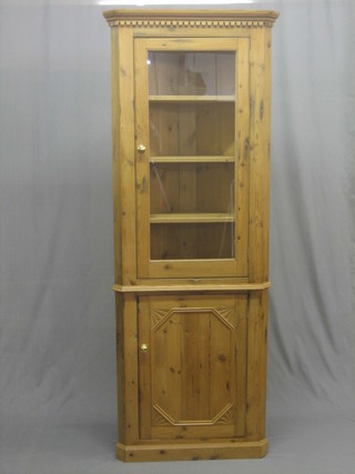 A 19th/20th Century pine double corner cabinet with moulded and dentil cornice, the interior fitted shelves enclosed by a glazed panelled door 29"