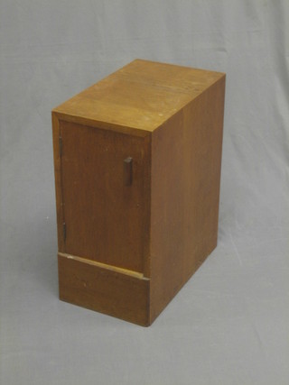 A 1930's Heales style oak pedestal bedside cabinet enclosed by a panelled door, raised on a platform base 12"