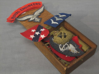 A small wooden box containing a General's wire cap badge, 5 Royal Engineers cloth shoulder titles,  "Luftwaffe" wings etc