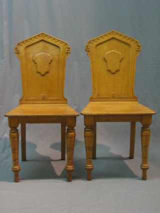 A pair of Victorian honey oak hall chairs with solid seats and backs, raised on turned supports
