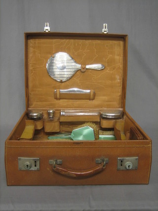 A leather vanity case containing 4 cut glass dressing table jars, a silver backed hand mirror, hair brush and comb, Birmingham 1908 together with a 5 piece silver and green enamelled backed dressing table set comprising pair of hair brushes, pair of clothes brushes and a hand mirror