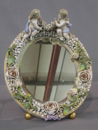 An oval plate easel mirror contained in a Meissen style floral encrusted frame supported by 2 cherubs 12"