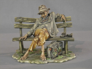 A Capo di Monte figure in the form of a reclining Tramp on a park bench 9"