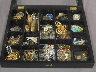 A glazed cabinet containing a collection of various costume jewellery, mostly brooches