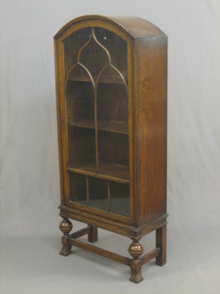 A 1930's Art Deco arch shaped oak display cabinet, the interior fitted adjustable shelves enclosed by astragal glazed panelled doors raised on turned and block supports 23"