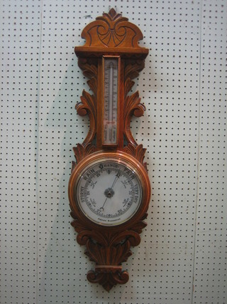 An aneroid barometer and thermometer with enamelled dial contained in a carved oak wheel case