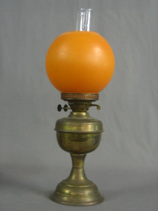A brassed finished oil lamp with orange glass shade
