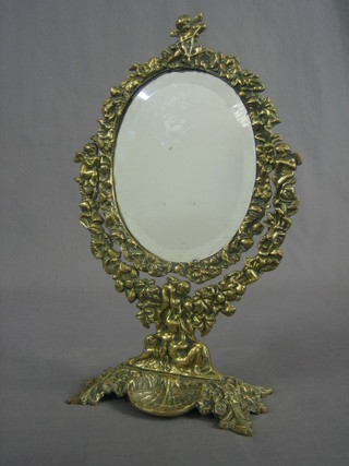 An oval bevelled plate easel mirror contained in a decorative polished brass frame surmounted by a figure of Cupid 16" 