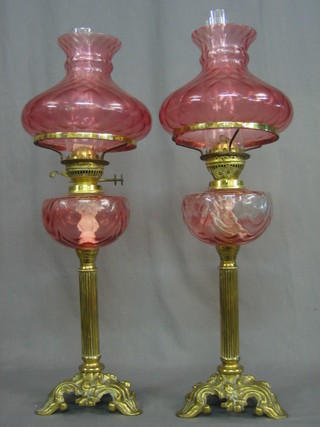 A pair of Victorian style oil lamps raised on reeded brass columns, complete with red glass shades and clear glass chimneys