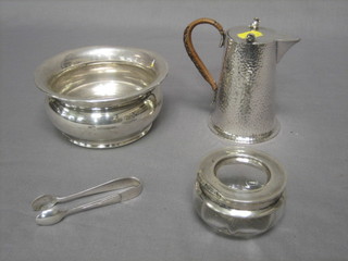 A planished silver plated hotwater jug, a circular silver plated bowl, a pair of silver sugar tongs and a circular glass bowl with silver rim