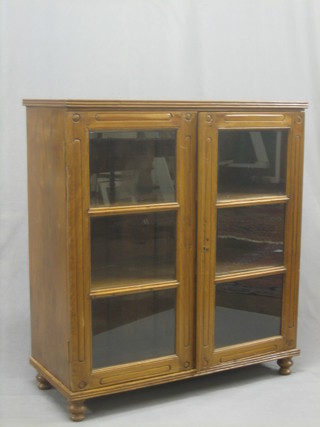 A Victorian style Eastern hardwood bookcase the interior fitted shelves enclosed by glazed panelled doors, raised on bun feet 36"