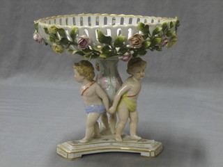 A Continental circular pierced porcelain table centre piece with floral encrusted decoration supported by 3 cherubs, raised on a triform base, 9"