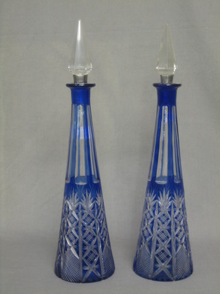 A pair of tall blue overlay glass cylindrical tapering decanters and stoppers (stoppers f and r)